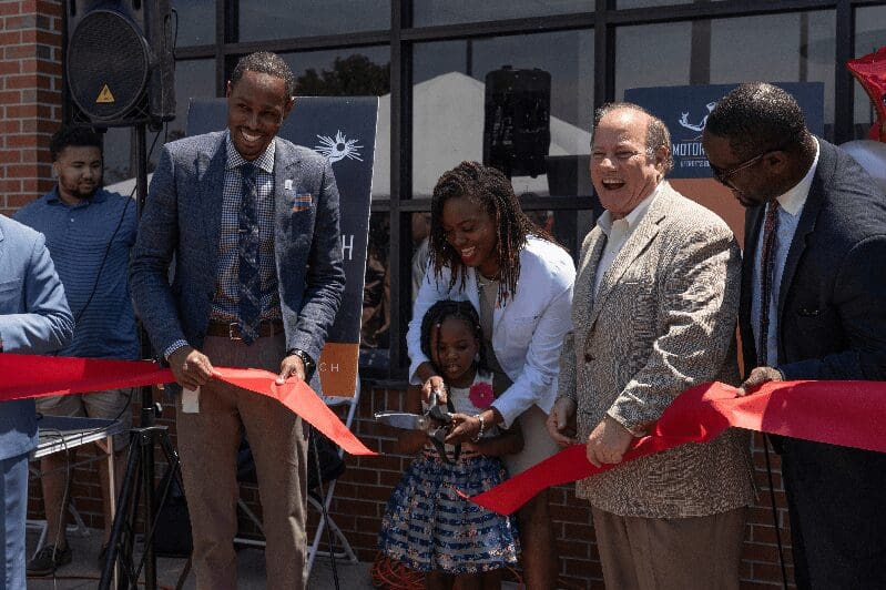 People celebrating an opening of a new business as a little girl cuts the ribbon