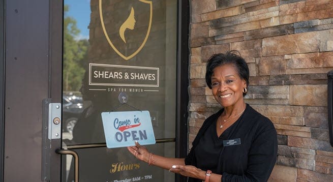A woman showcasing the open sign on the front door of her business